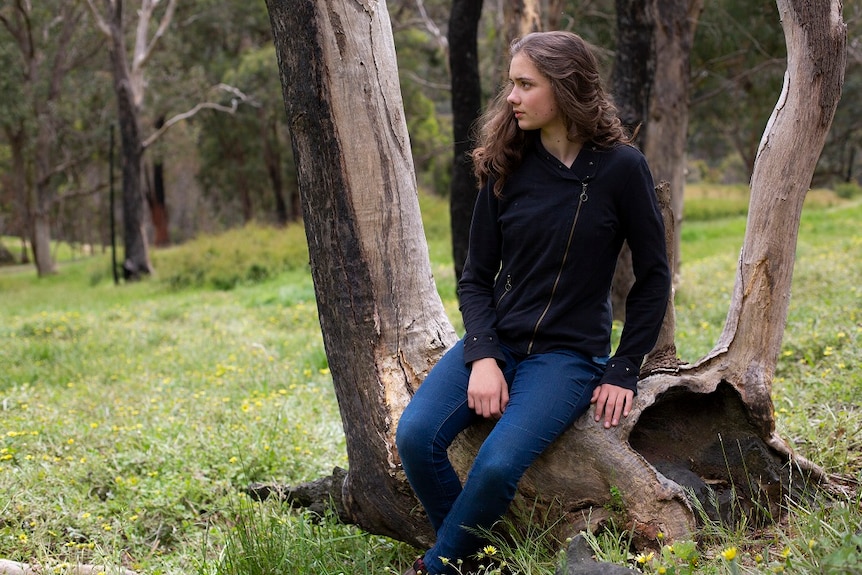 A young girl sits on a log and looks away