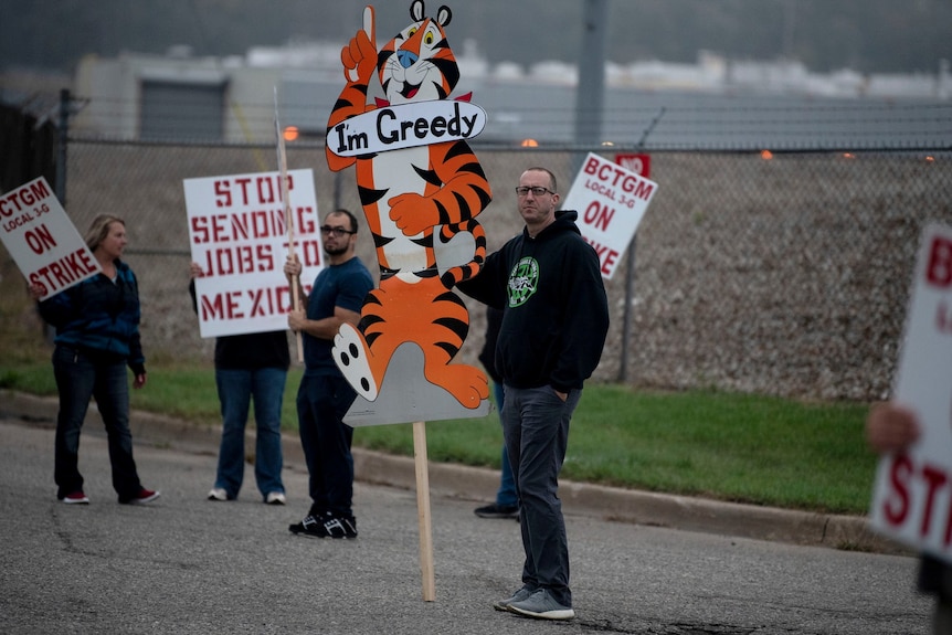 A man holding a cardboard cut-out of the lion mascot with "I'm Greedy" written on it 