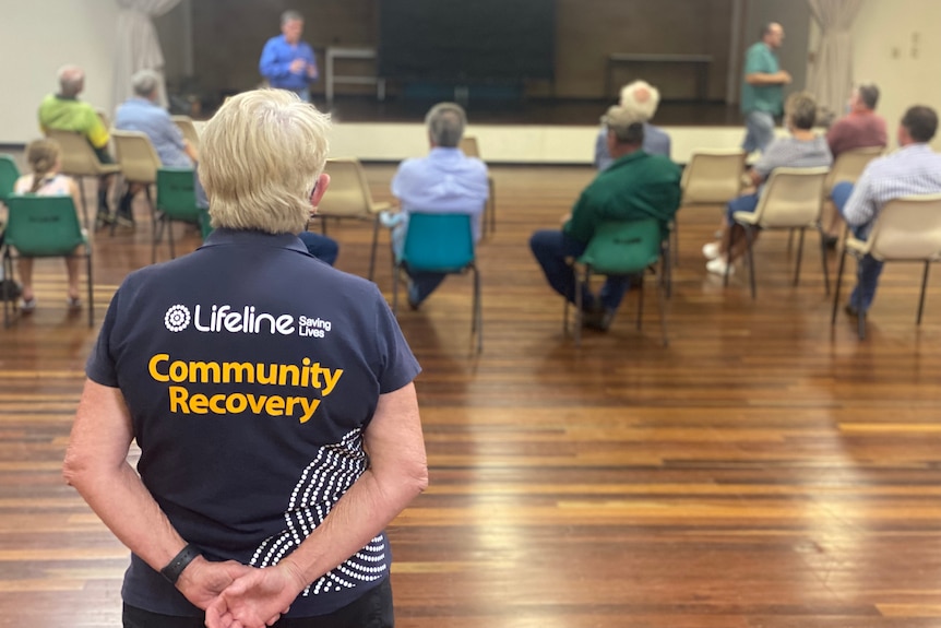 A Lifeline volunteer watches on as a group of people sit around inside a community hall.