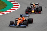 An orange McLaren F1 car rounds a bend followed by a Red Ball car.