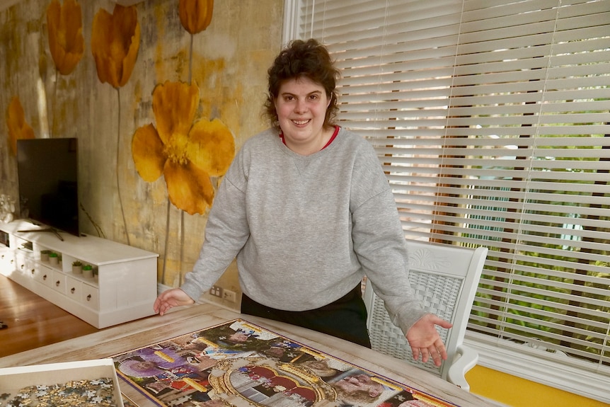 Chloe Osmond smiling and standing behind a table, on which sits a nearly-completed jigsaw puzzle featuring the Royal family.