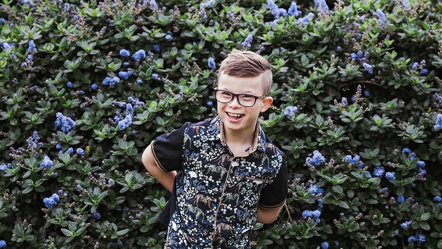 Felix Paskett smiles in front of flowers, wearing a button up shirt and glasses.