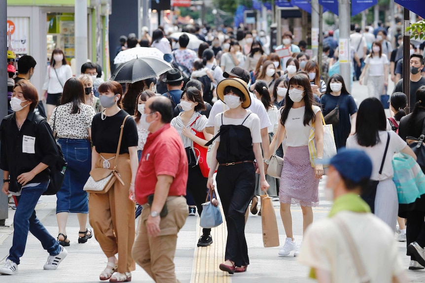People wearing face masks walk along a busy street in the sunshine
