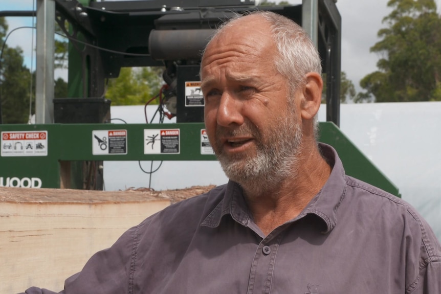 Photo of a man talking in front of a tree mill.