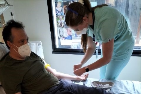 a photo of a man in a hospital bed with a nurse putting something in his arm 