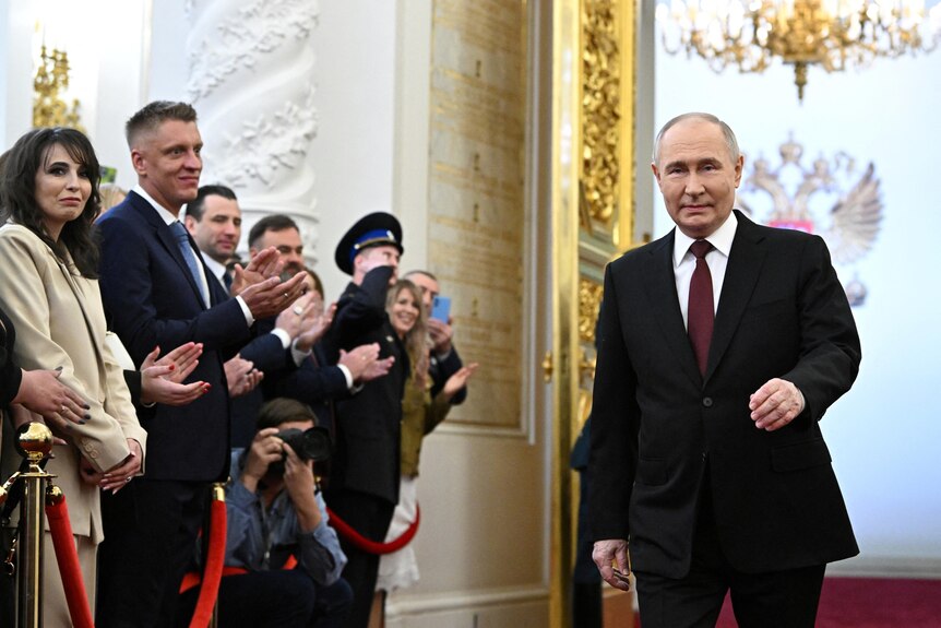 Vladimir Putin walks down a red carpet past a crowd who are clapping him