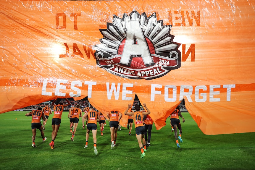 GWS players run through an Anzac Day banner with the words 'Lest We Forget'. 