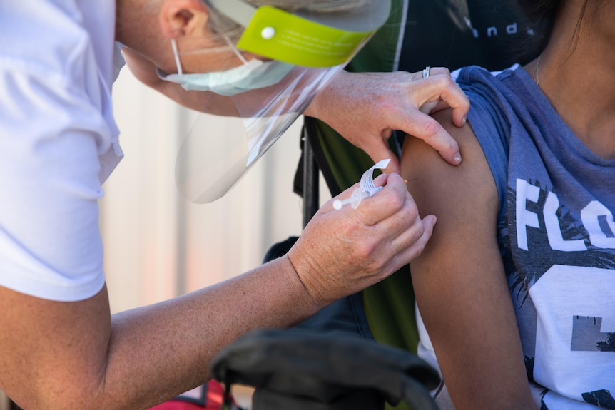 A woman receives a vaccine while sitting in a camping chair on a driveway.