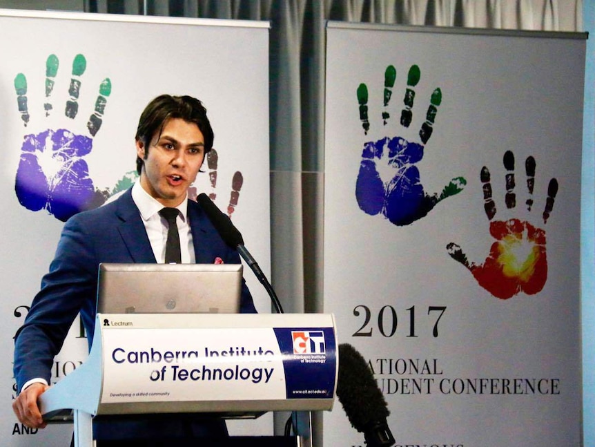 An Indigenous man at a podium talks to a group of students.