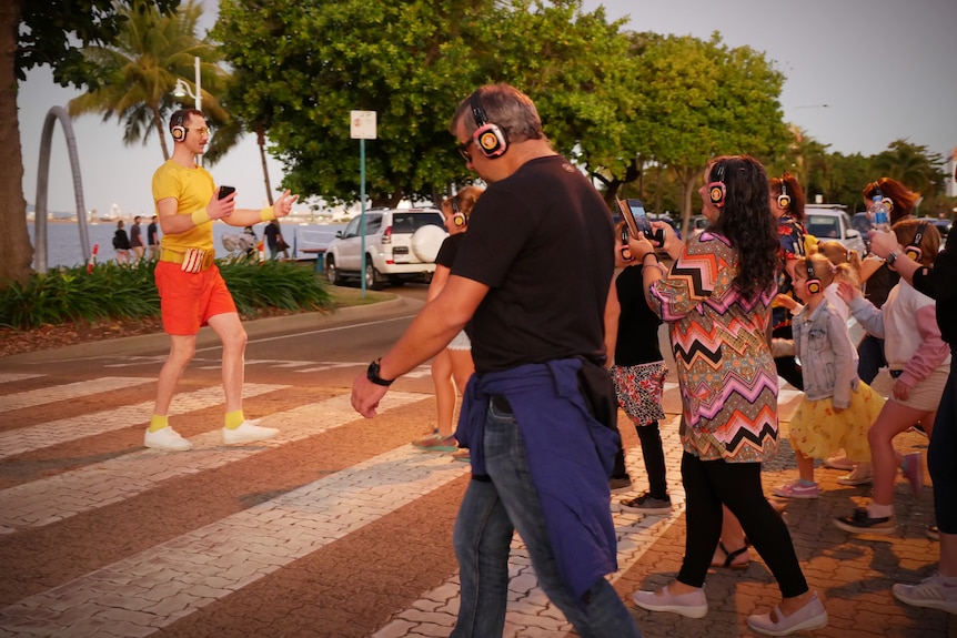 A group of people wearing headphones follow a guide as they cross the road towards the ocean