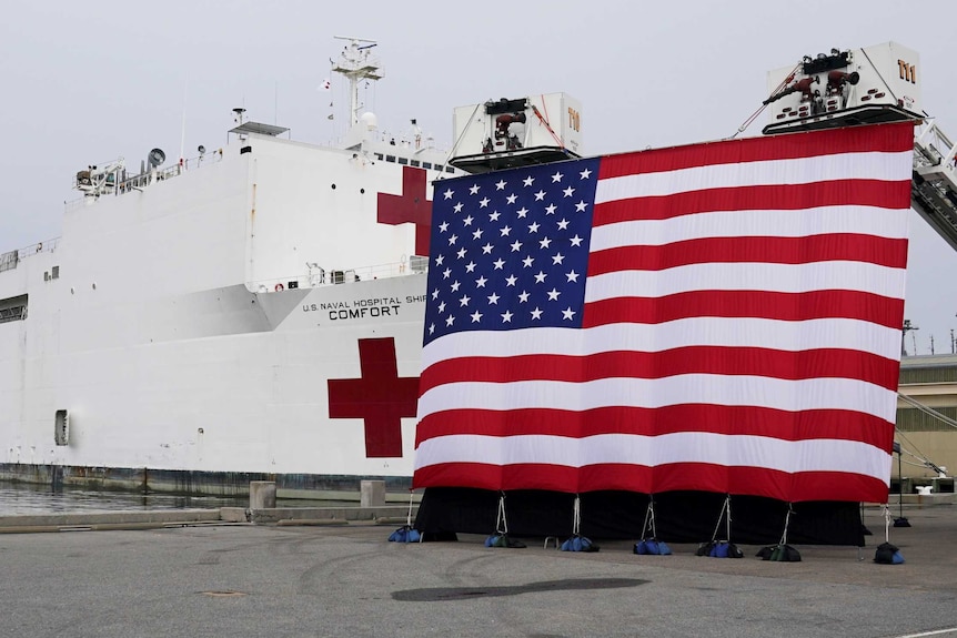 A massive flag is raised next to a hospital ship with a red cross on it