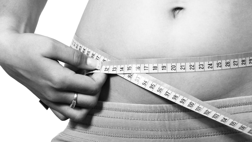 A woman measures her waist with tape.