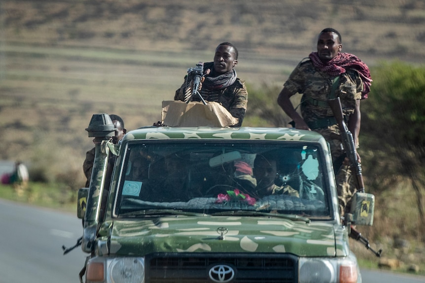 A 4WD with men in camouflage fatigues and with long arms standing on the tray. 