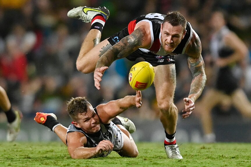 A St Kilda player tries to keep his balance as he pitches forward and reaches for the ball with a Power defender on the ground.