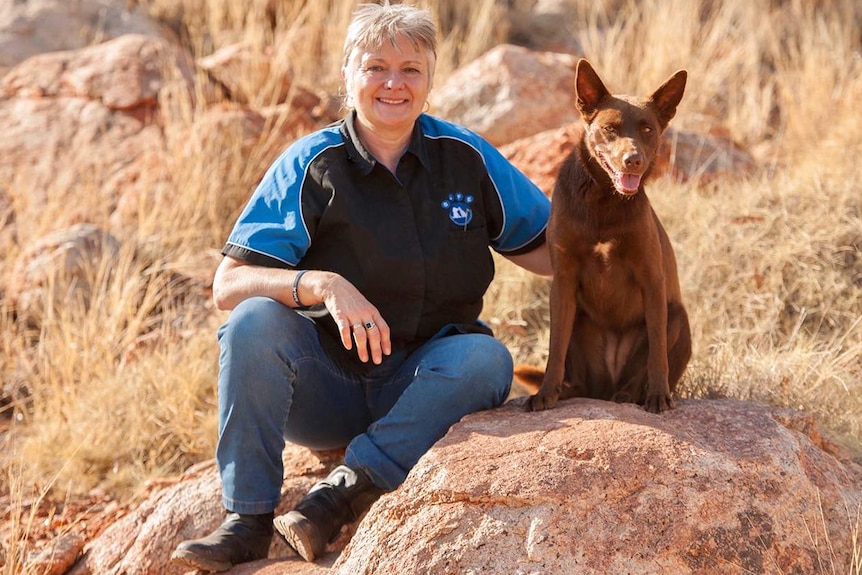 Sue Hedley sits on a rock with a working kelpie dog.