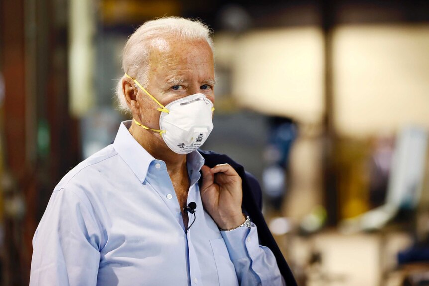Joe Biden in a face mask with his jacket slung over his shoulder