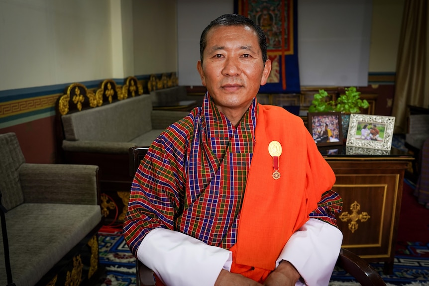 A man in traditional Bhutanese garb sits in an office