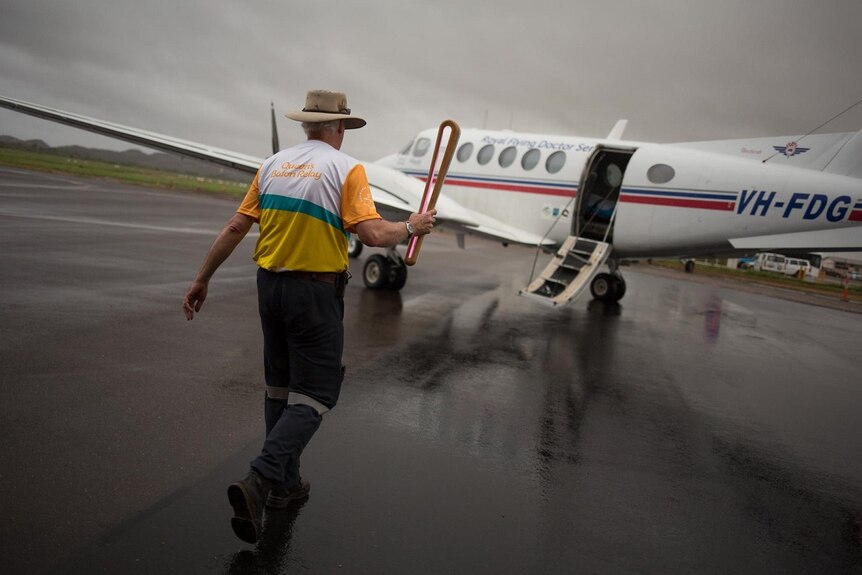 A man carries the Queen's Baton onto a Royal Flying Doctor Service flight on a rainy day