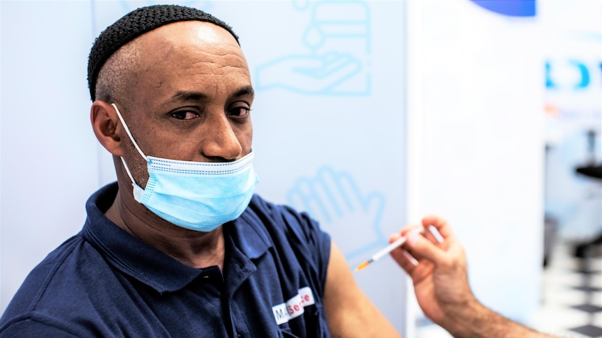 A man wearing a small black cap receives a dose of a COVID-19 vaccine 