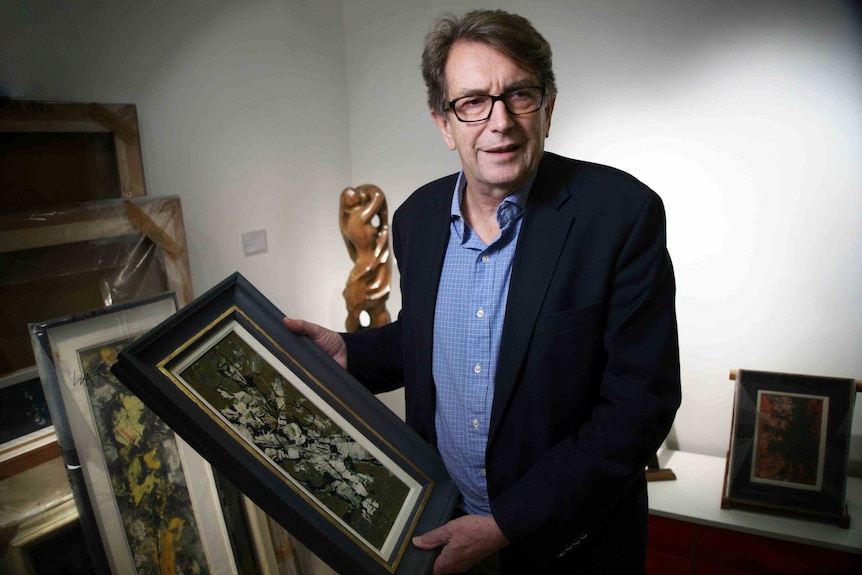 Australian art dealer Adrian Mibus holds a painting