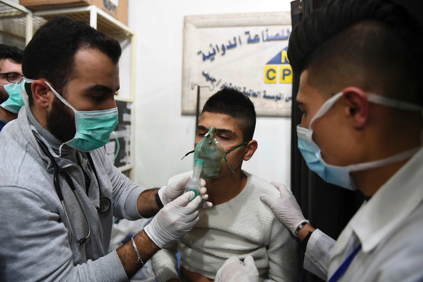 Two doctors tend to a young man wearing an oxygen mask.