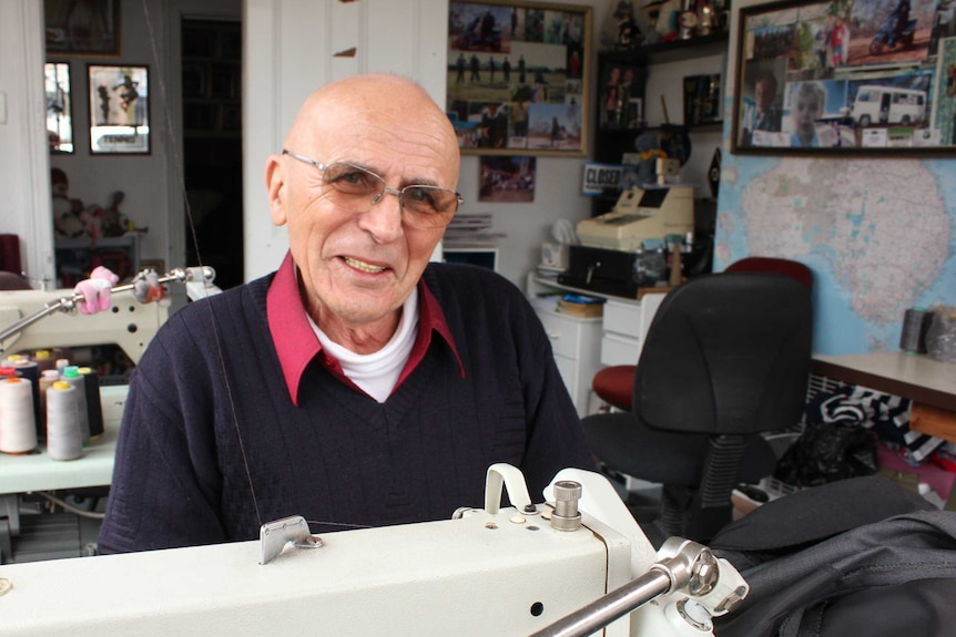 Matthew Kelava sits behind a sewing maching at his alterations shop. with reels of cotton in the background.