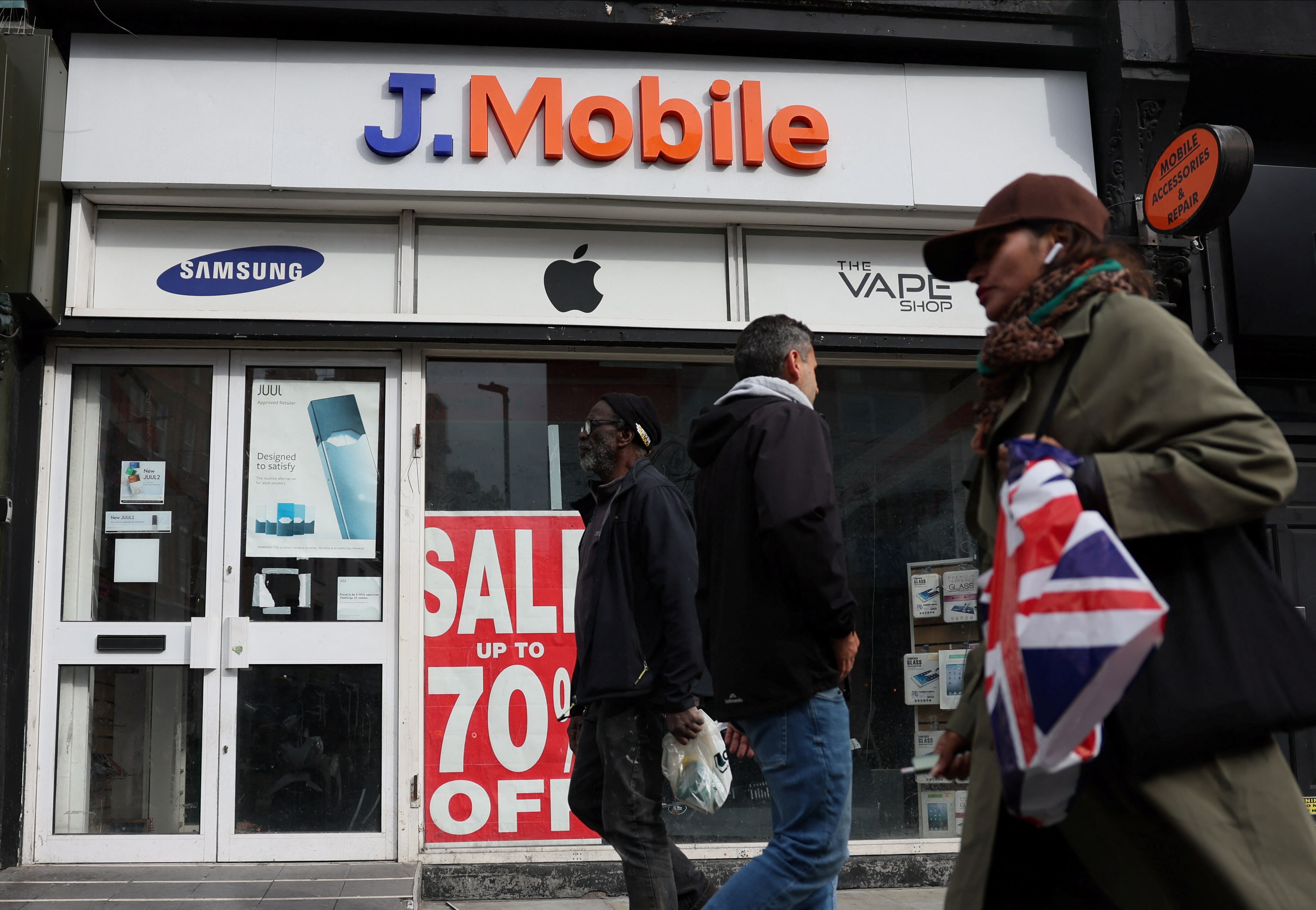 Non-descript shoppers walking past a discount store on a UK high street.
