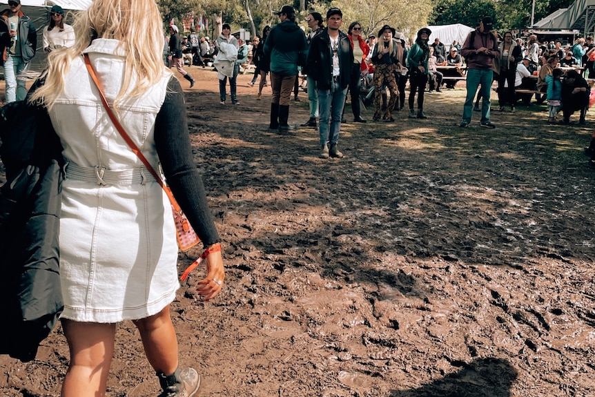 A woman and crowds walk through muddy grounds at a music festival