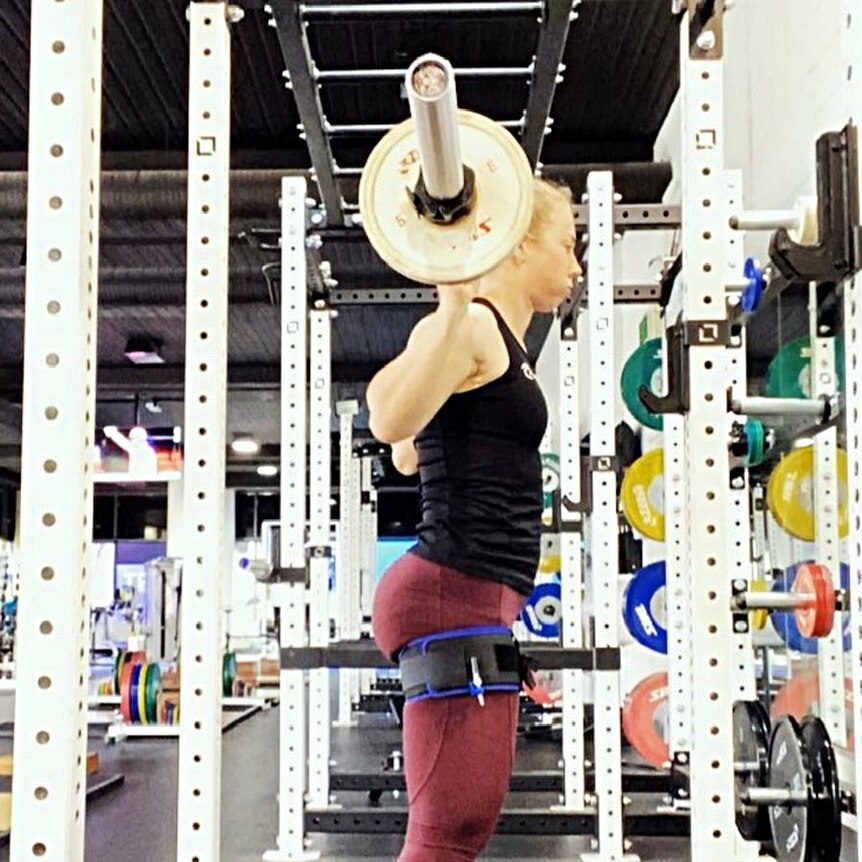 Womn with heavy bar on her back as part of squat routine