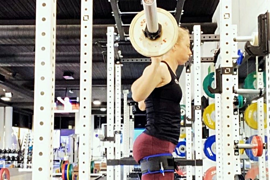 A woman with in the gym with a heavy bar on her back as part of a squat routine.