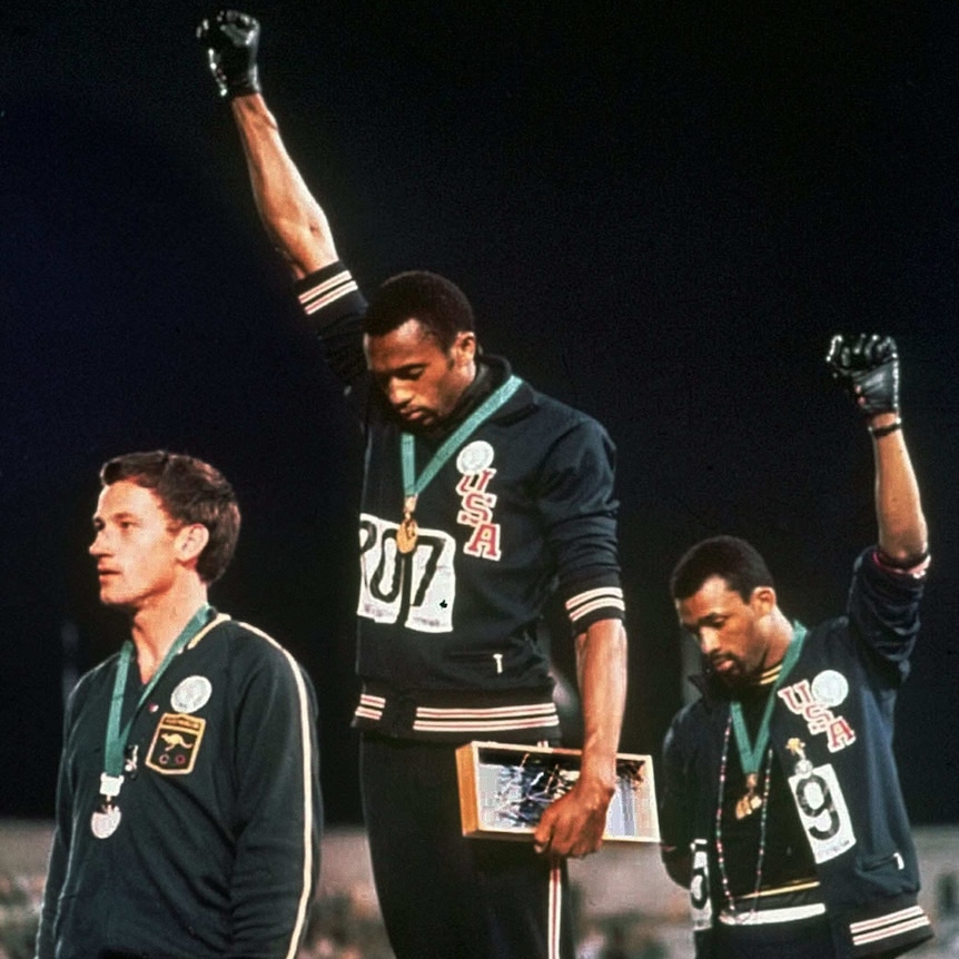 Tommie Smith, centre, and John Carlos stare downward while extending gloved hands skyward