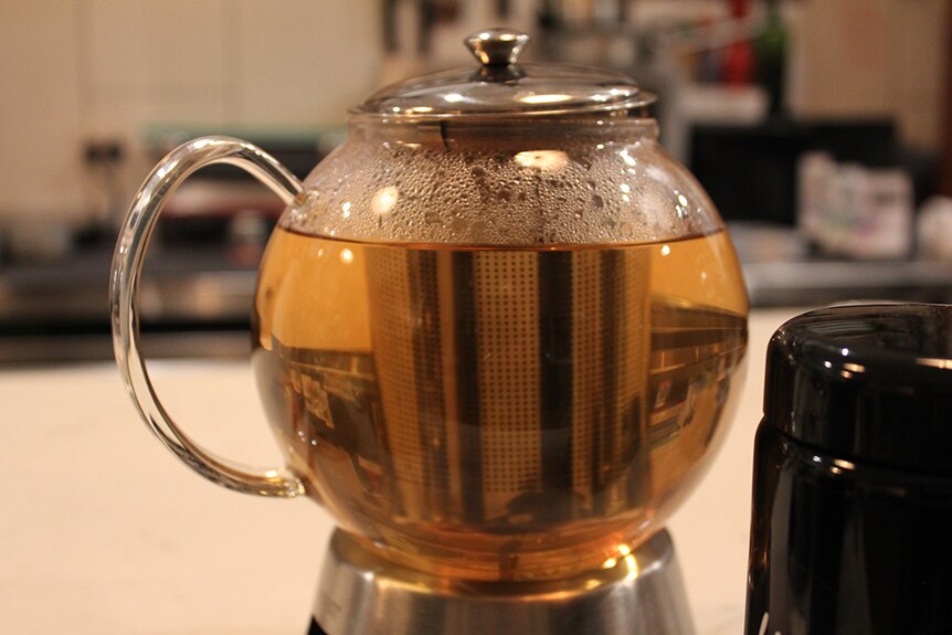 Loose leaf tea steeping in a metal canister inside a clear glass teapot.