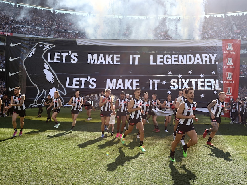 Magpies AFL player run through their banner at the AFL grand final.