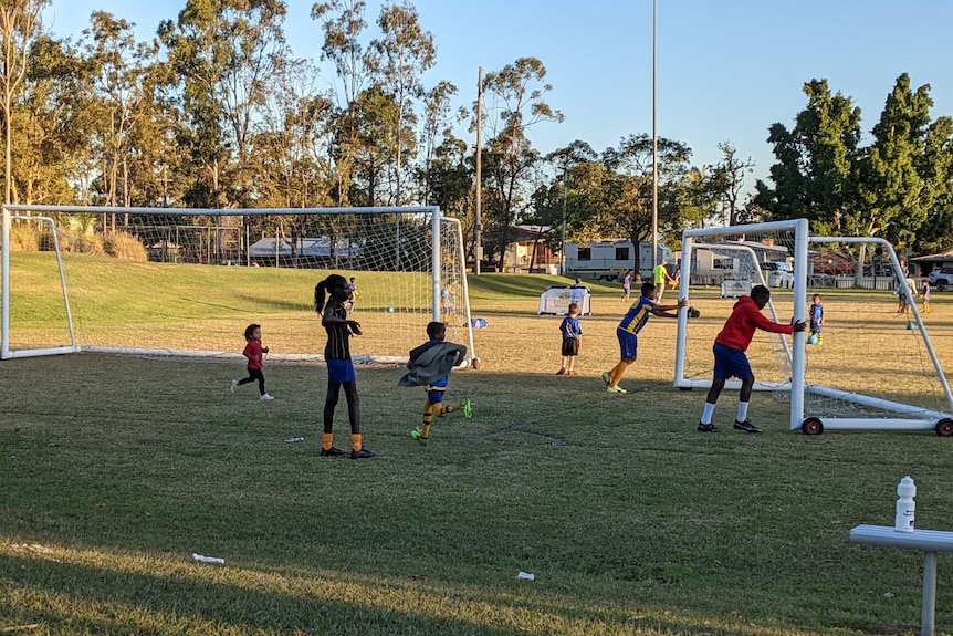 Some boys push a goal frame while a girl stands in the foreground.