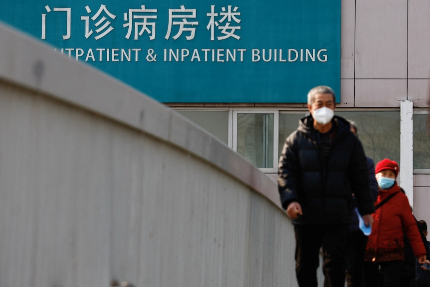 People wearing masks on a bridge, while a big sign behind them says "outpatient and inpatient building"