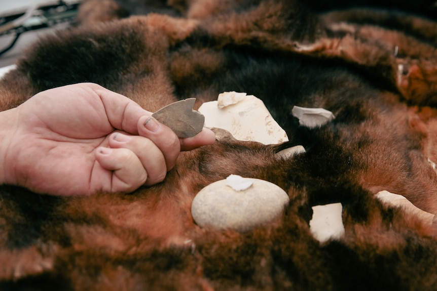 Aboriginal stone artefacts held by hand on top of possum skin cloak