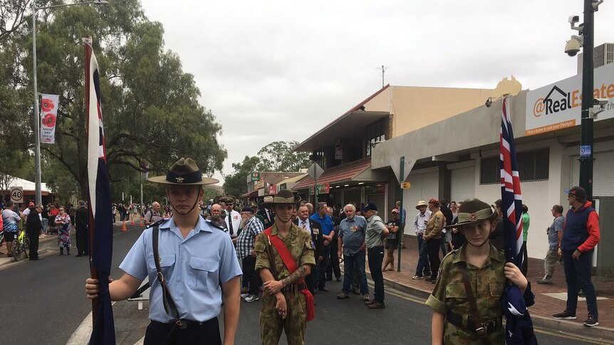 Two servicemen and one servicewoman standing in uniform with Australian flags before the march.