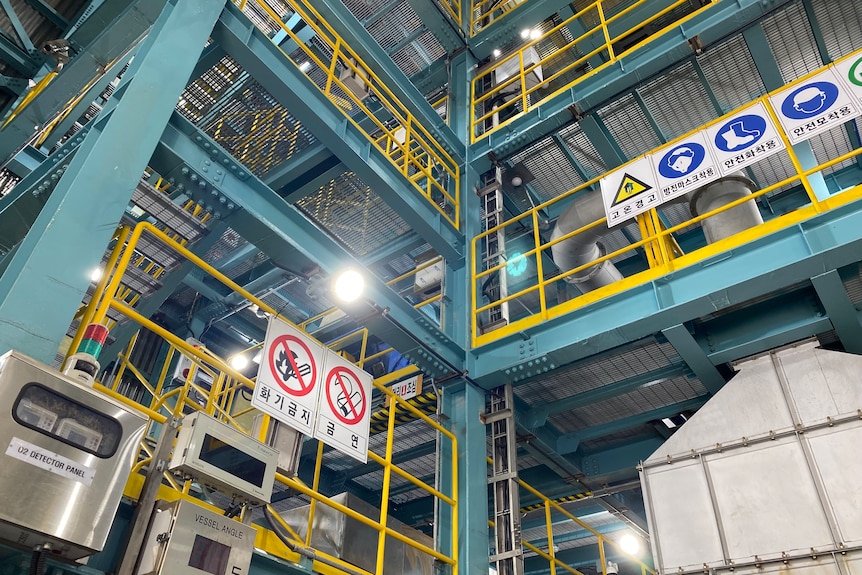A large factory with blue steel beams and yellow safety railings surrounded by safety signs.