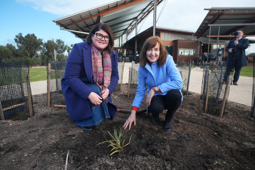Zoe Bettison and Susan Close crouch down in a garden bed outside the centre