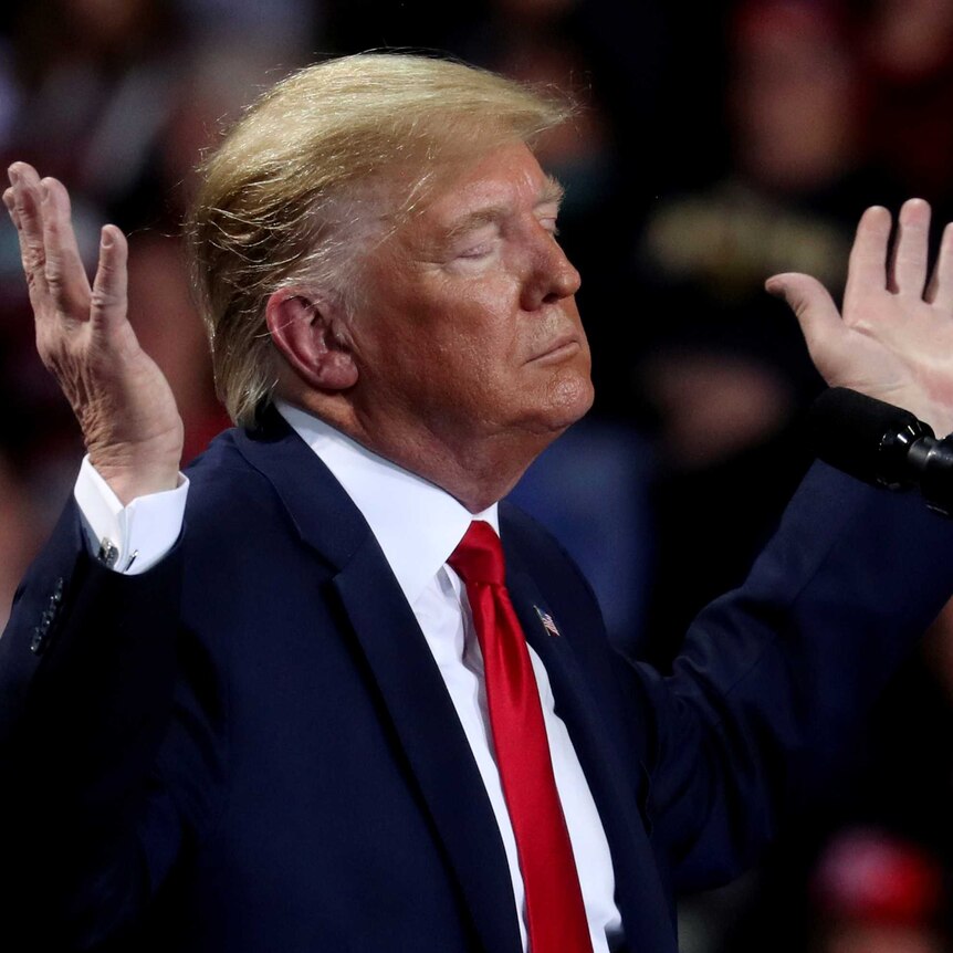 Donald Trump raises both hands in the air, his eyes closed.