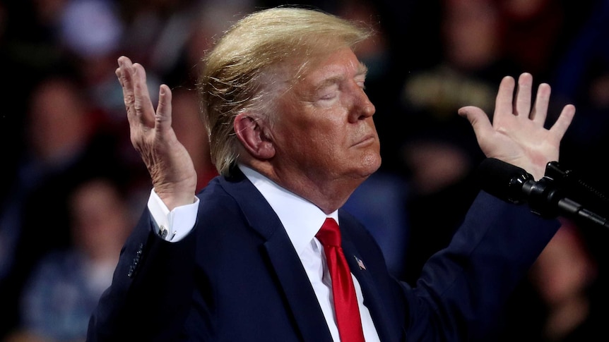 Donald Trump raises both hands in the air, his eyes closed.