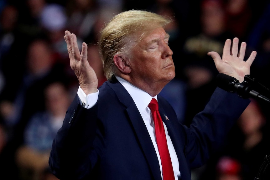 Donald Trump with his eyes closed and his hands thrown to the heavens
