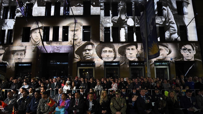 The faces of servicemen can be seen projected onto a building.