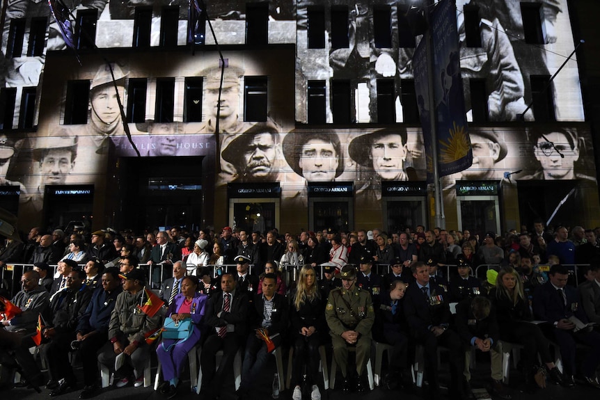 The faces of servicemen can be seen projected onto a building.