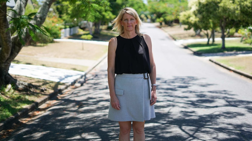 Julie Gilbert stands on a street under a fig tree in Brisbane.