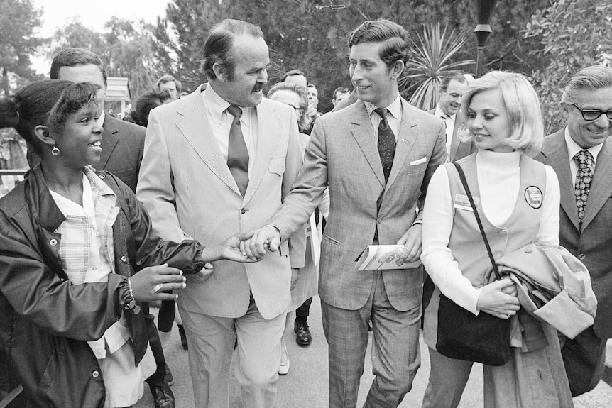 Prince Charles dressed in a suit and tie greets a woman while walking