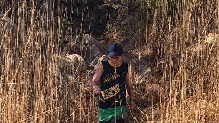 A boy walks over boulders through tall brown grass