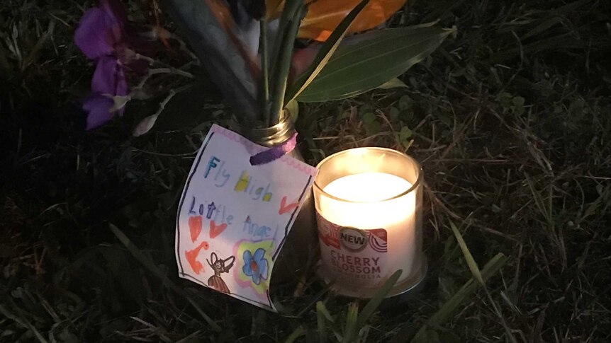 A note that reads "Fly High Little Angel" is a attached to a small glass of flowers, next to a candle.