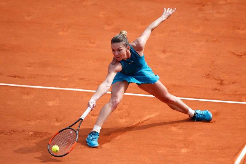 Romanian tennis player Simona Halep leans forward to reach for ball on clay court