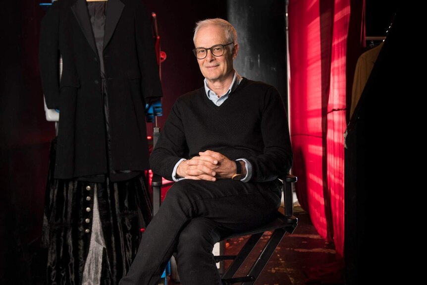 A man sits on a director's chair backstage at the theatre